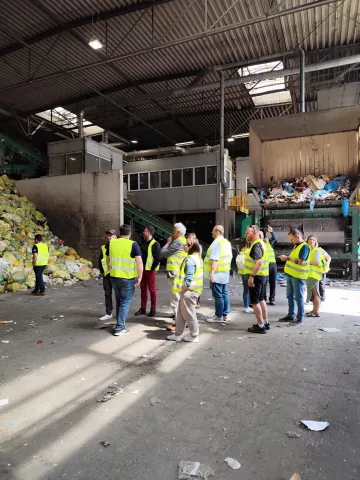 ludzie w kamizelkach odblaskowych w sortowni odpadów