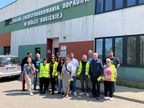 ludzie w kamizelkach odblaskowych przed budynkiem zakłądu gospodarowania odpadami
